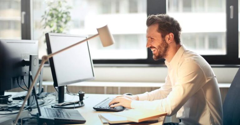 Pc - Man in White Dress Shirt Sitting on Black Rolling Chair While Facing Black Computer Set and Smiling