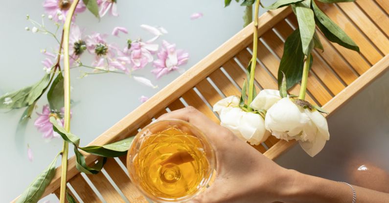 REST And SOAP - Top view of anonymous female with white wine sitting in bathtub with pink and white flowers